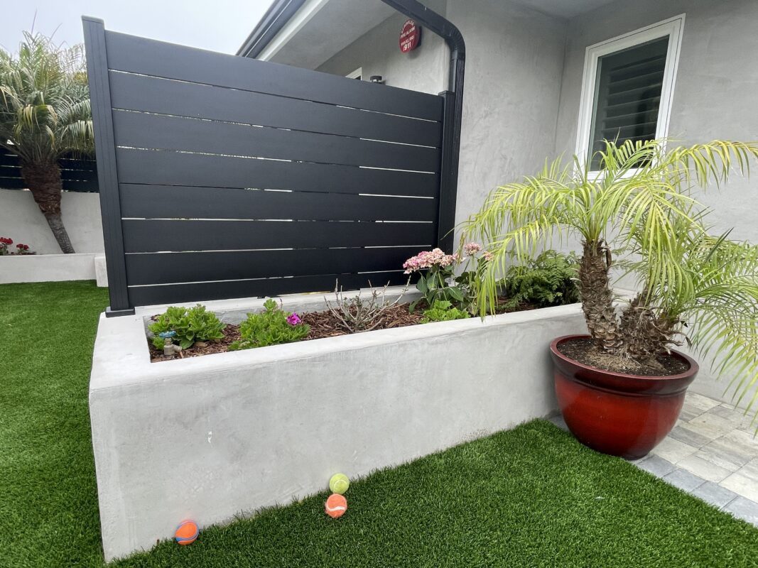 Modern black privacy wall installation complements a landscaped yard with vibrant plants.