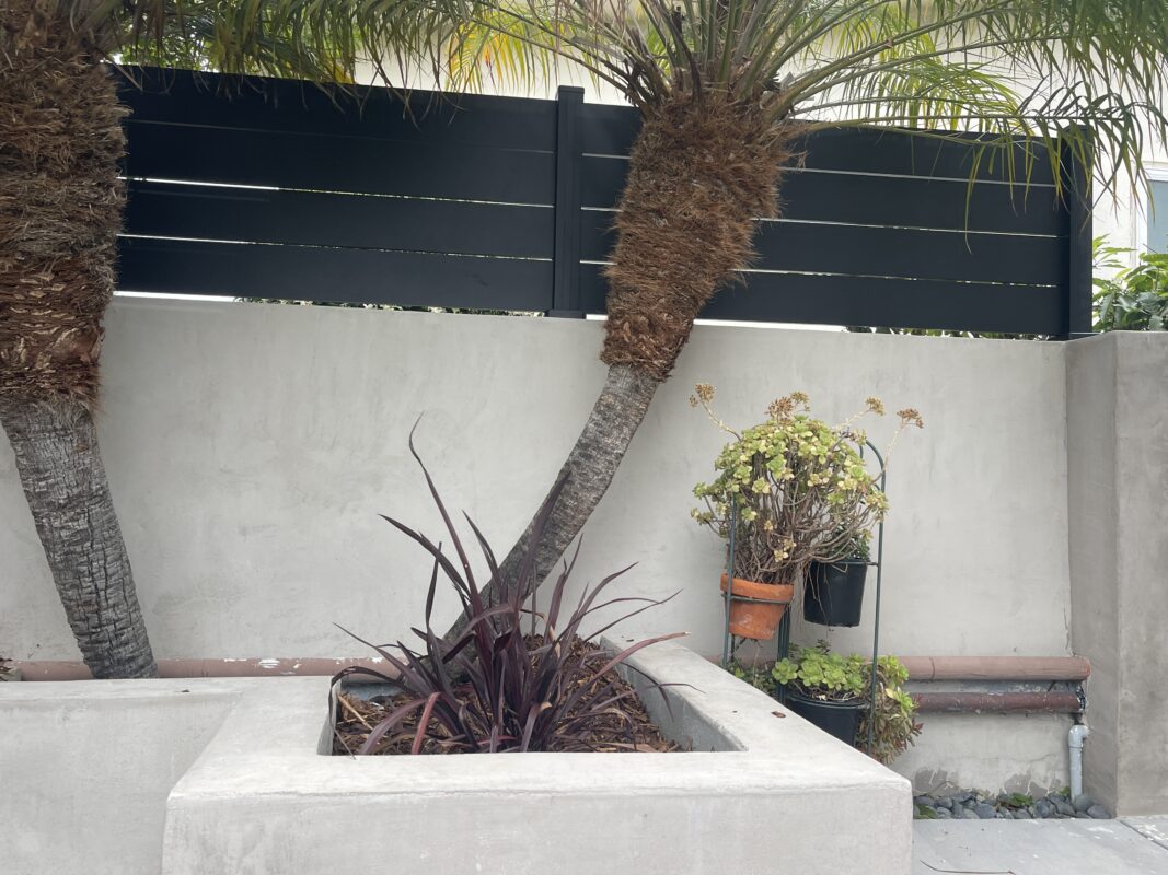 Modern black wall topper and privacy wall with palm trees and plants in a landscaped area.
