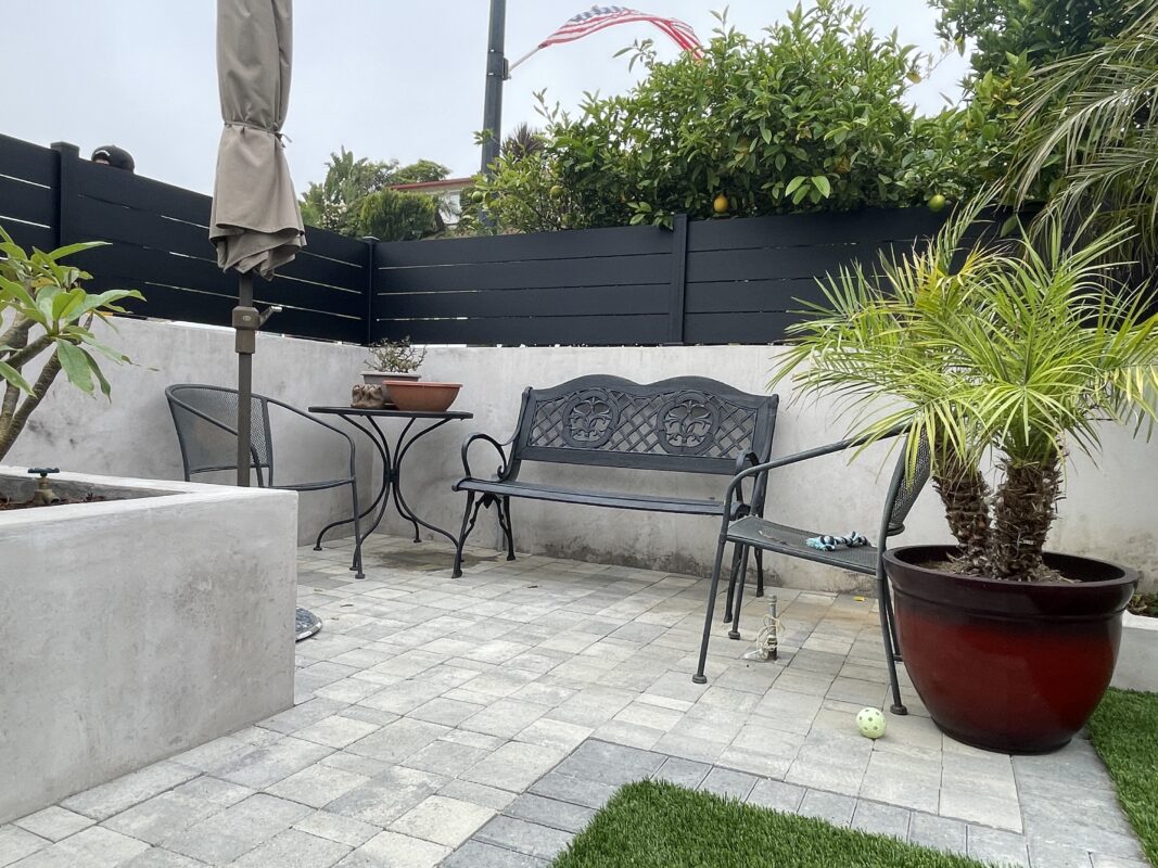 Modern black fence encloses a cozy outdoor seating area with potted plants and patio furniture.