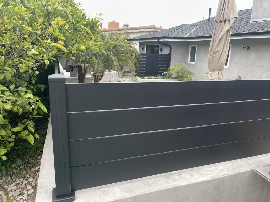 Modern black fence with wall topper, surrounded by greenery in a coastal home setting.