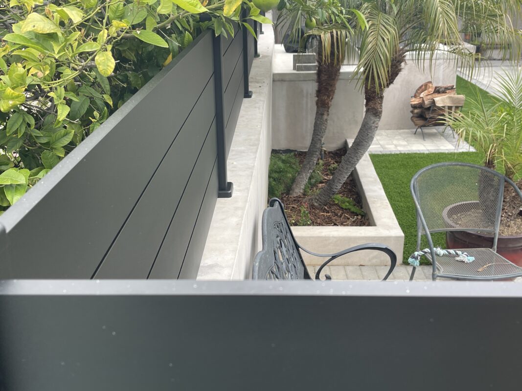 Close-up of a modern black wall topper beside greenery and a patio area.