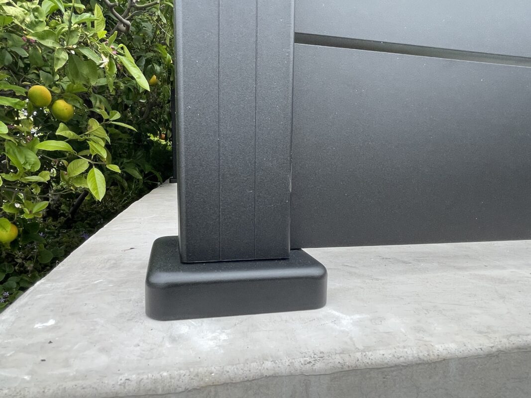 Close-up of a modern black fence post installed on a patio surrounded by greenery.