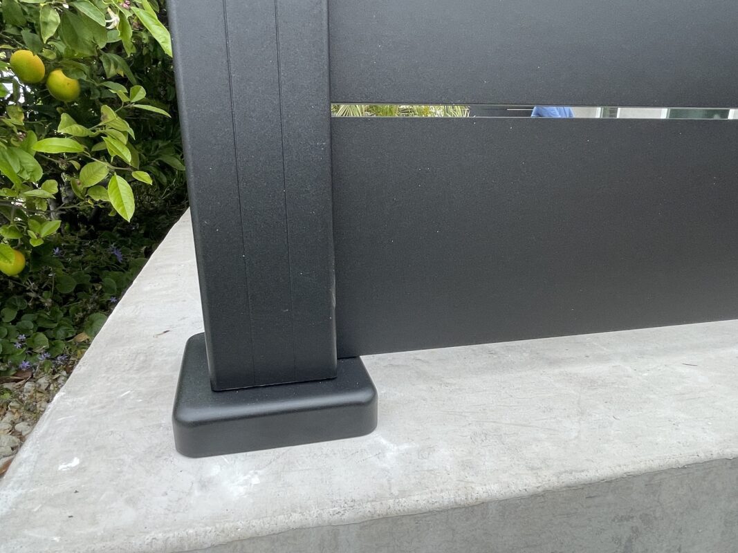 Close-up of a modern black fence installation with greenery in the background.