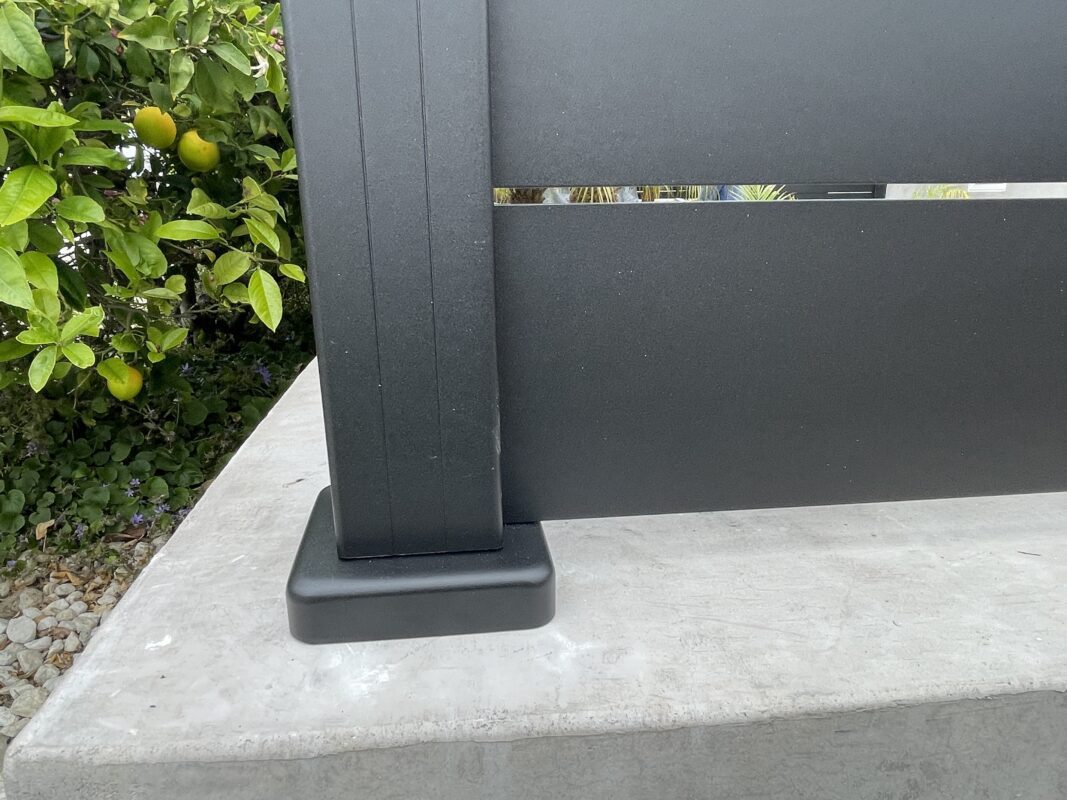 Close-up of a modern black fence installation with greenery in the background.