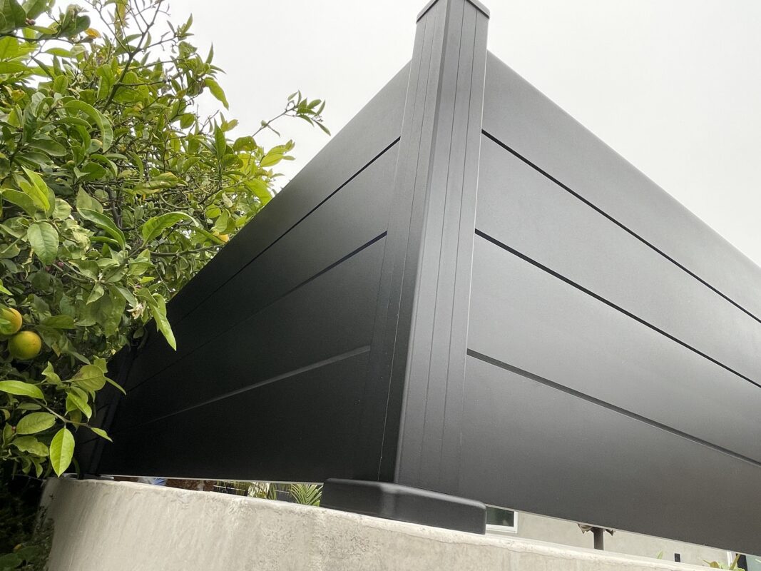 Close-up of a modern black wall topper installed alongside lush greenery.
