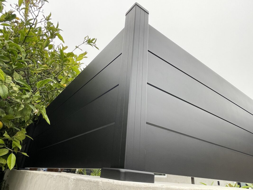Close-up of a modern black privacy wall with greenery in the background.