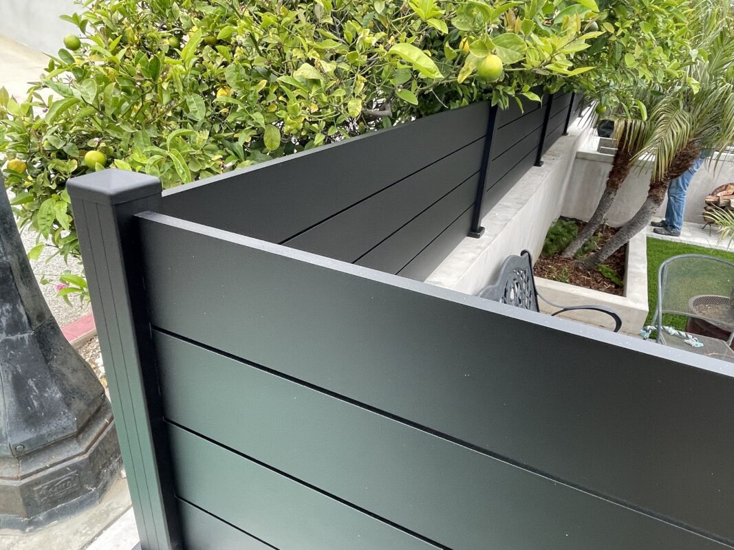 A modern black fence with greenery atop, enhancing the outdoor space's privacy and style.