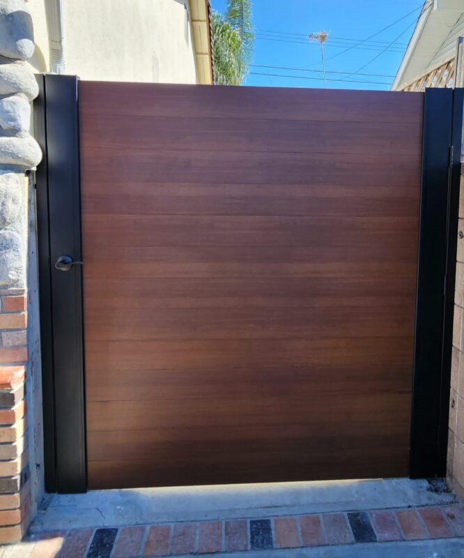 A modern full privacy gate with a wood-like finish, installed in a residential area.