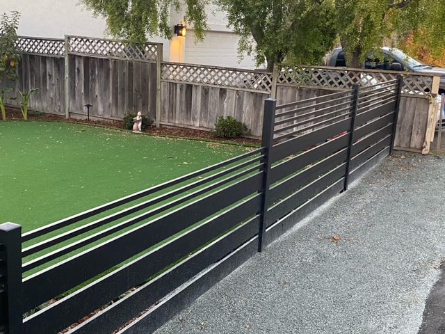 Installation of a sleek black aluminum fence beside a green lawn area.