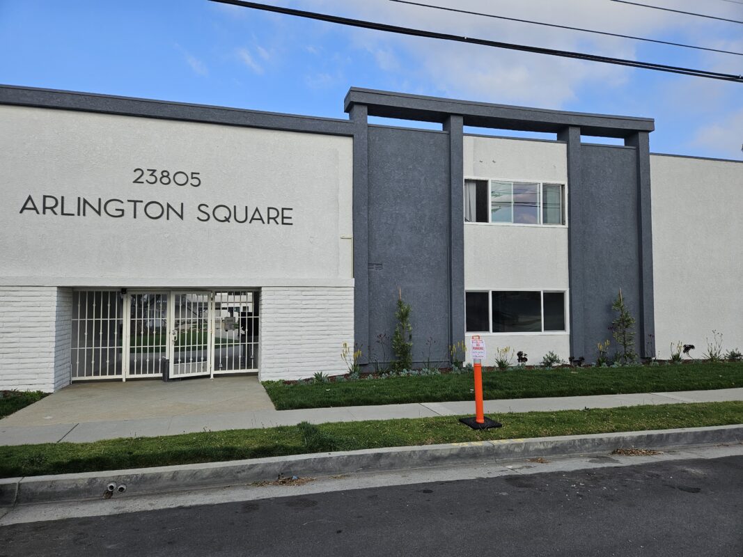 Photo of a modern building exterior with a gated entrance and landscaping.