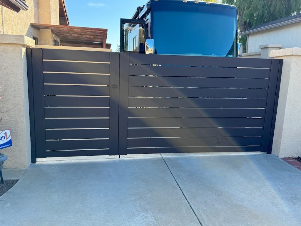 A sleek bronze gate installed beside a concrete driveway in a residential area.