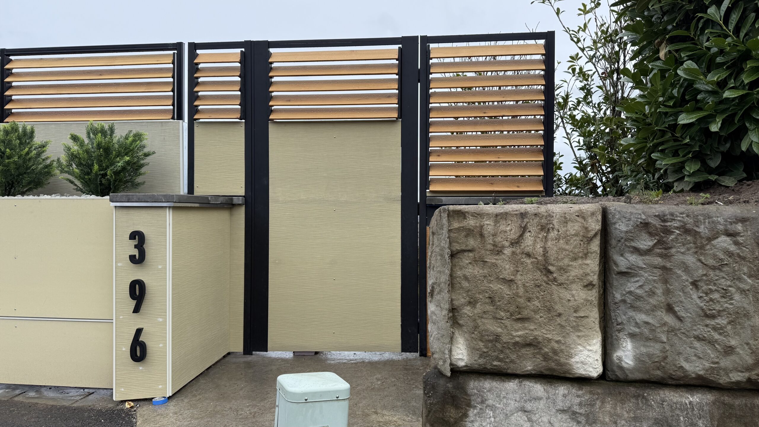 A modern driveway gate with horizontal slats, surrounded by greenery and stone accents.