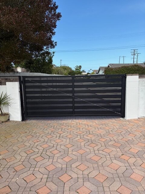 A sleek black driveway gate installed in a residential area with a patterned pavement.