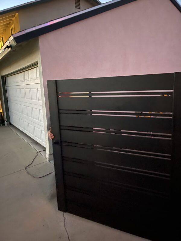 A black aluminum double swing gate being installed next to a garage.